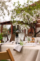 Photo of Stylish table setting with beautiful spring flowers, wine, plates and glasses in garden