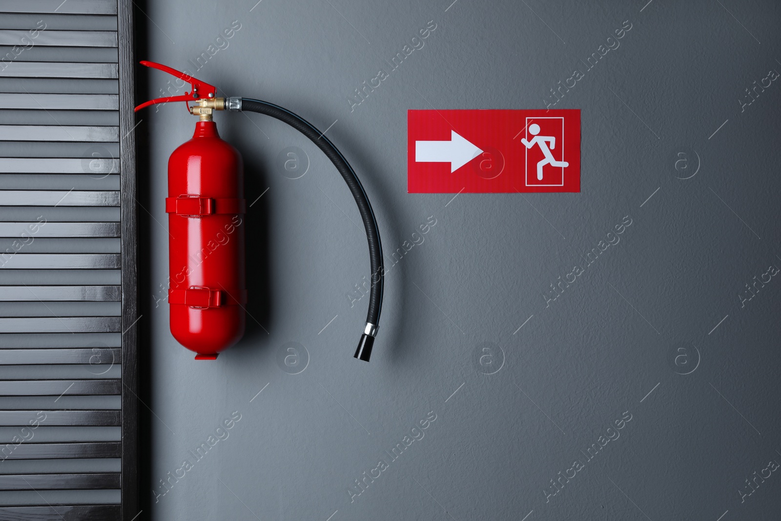 Photo of Fire extinguisher and emergency exit sign on grey wall indoors