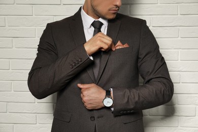 Photo of Man fixing handkerchief in breast pocket of his suit near white brick wall, closeup