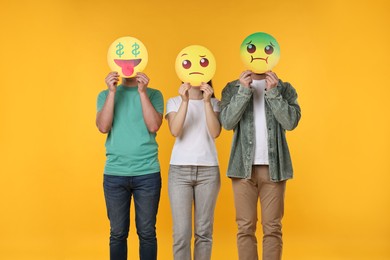 People covering faces with emoticons on yellow background