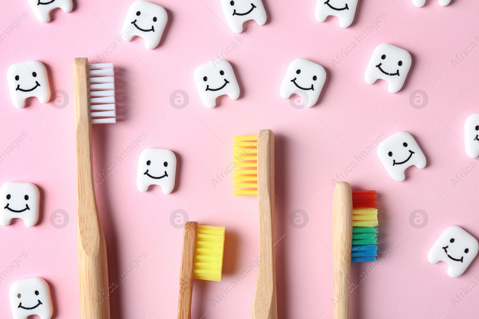 Photo of Small plastic teeth with happy faces and wooden brushes on color background, flat lay