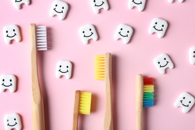 Small plastic teeth with happy faces and wooden brushes on color background, flat lay