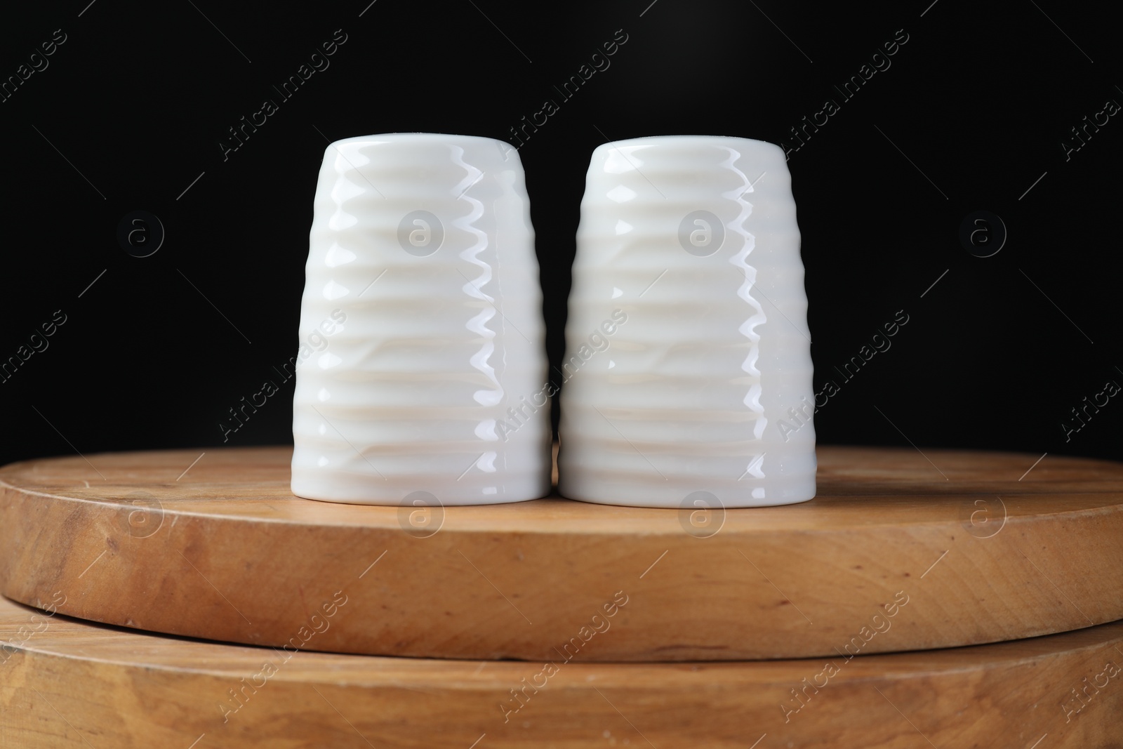 Photo of Salt and pepper shakers on wooden boards against black background, closeup