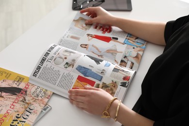 Photo of Woman reading fashion magazine at white table, closeup