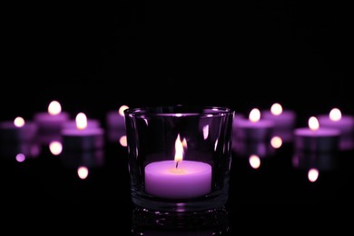 Image of Burning violet candle on black background, closeup. Funeral attributes