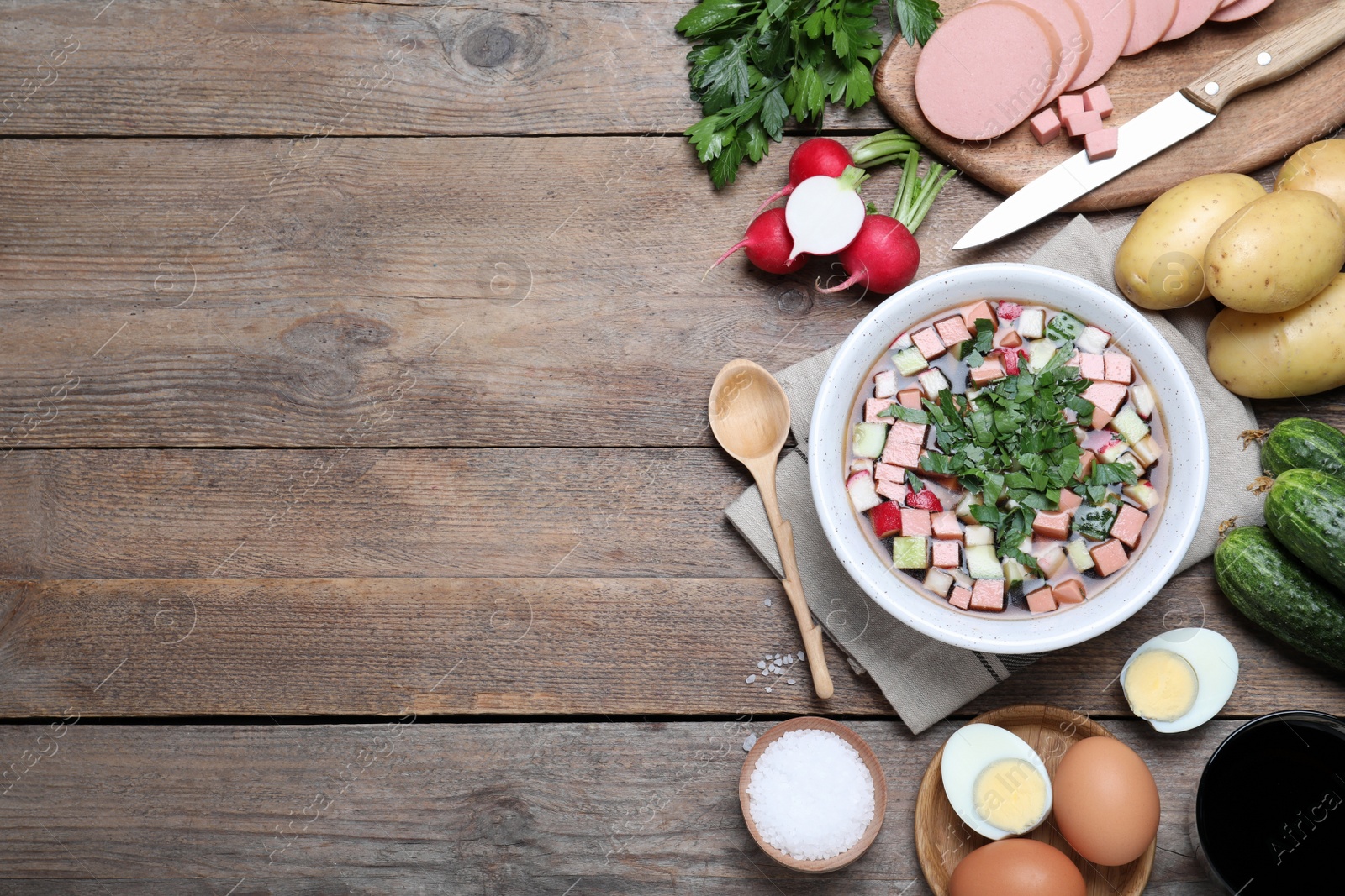 Photo of Flat lay composition of okroshka with kvass and ingredients on wooden table, space for text. Traditional Russian summer soup