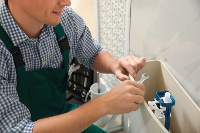 Photo of Professional plumber repairing toilet in bathroom, closeup