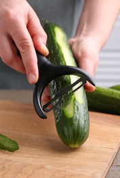 Photo of Woman peeling cucumber at wooden table indoors, closeup