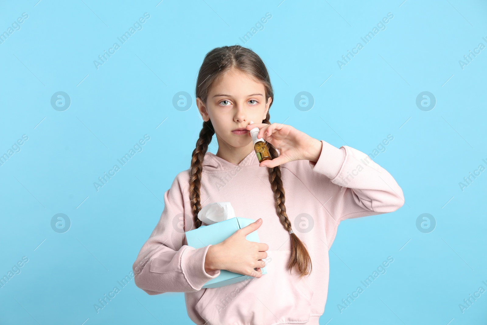 Photo of Sick little girl using nasal spray on light blue background