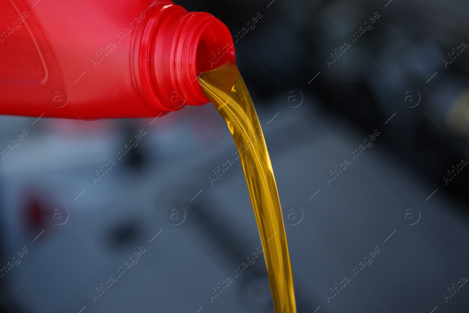 Photo of Pouring motor oil from red container against blurred background, closeup