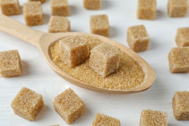 Photo of Brown sugar cubes in spoon on white wooden table, closeup