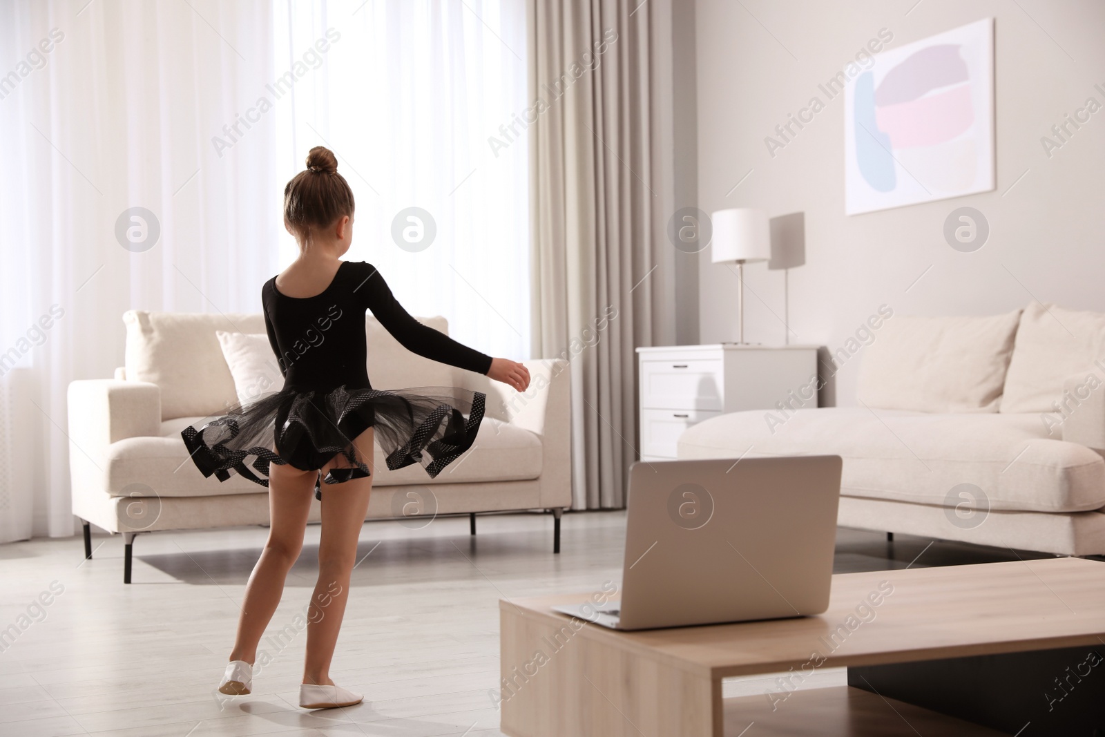 Photo of Cute little girl taking online dance class at home, back view