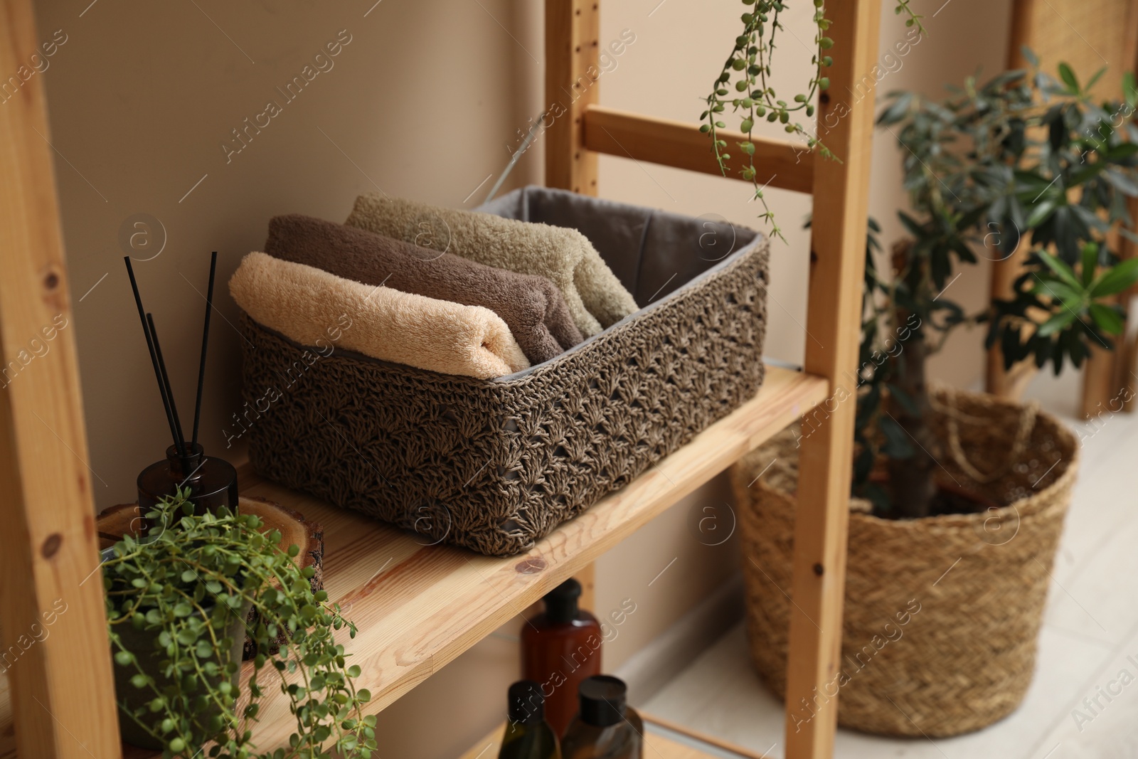 Photo of Soft towels in storage box, plants and bottles on shelves indoors