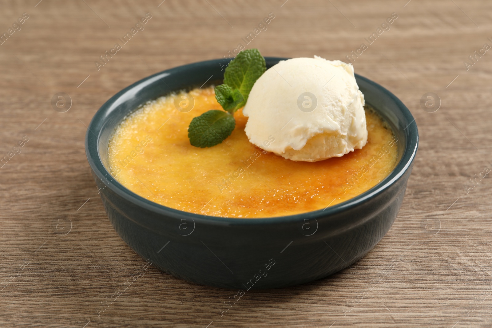 Photo of Delicious creme brulee with scoop of ice cream and mint on wooden table, closeup
