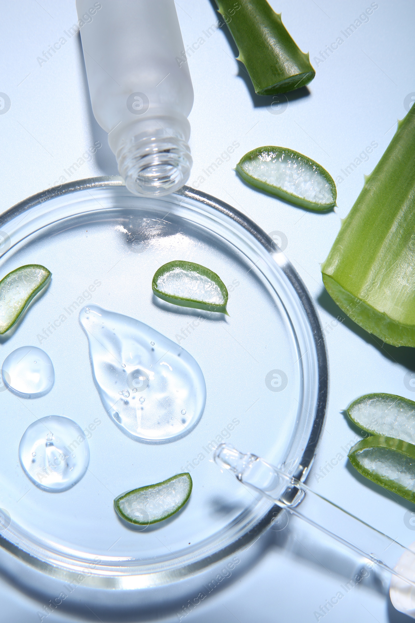 Photo of Cut aloe vera, bottle and drops of cosmetic gel on light blue background, flat lay