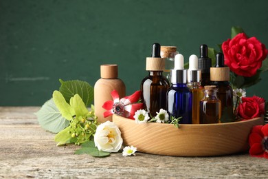 Photo of Aromatherapy. Different essential oils, flowers and green leaves on wooden table