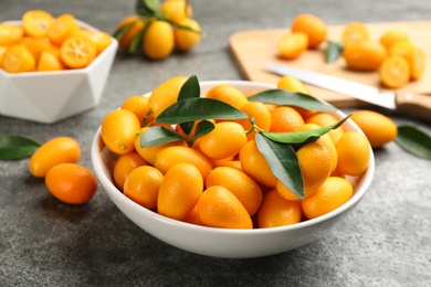 Fresh ripe kumquats in bowl on grey table