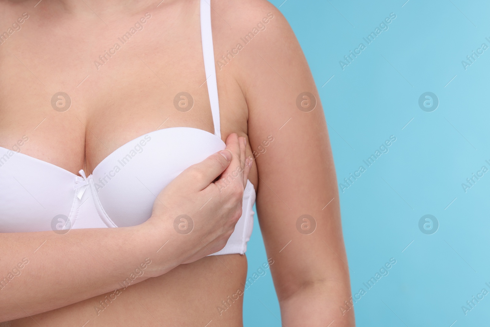 Photo of Mammology. Woman in bra doing breast self-examination on light blue background, closeup