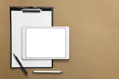 Modern tablet, stylus, pen and clipboard on light brown background, flat lay. Space for text