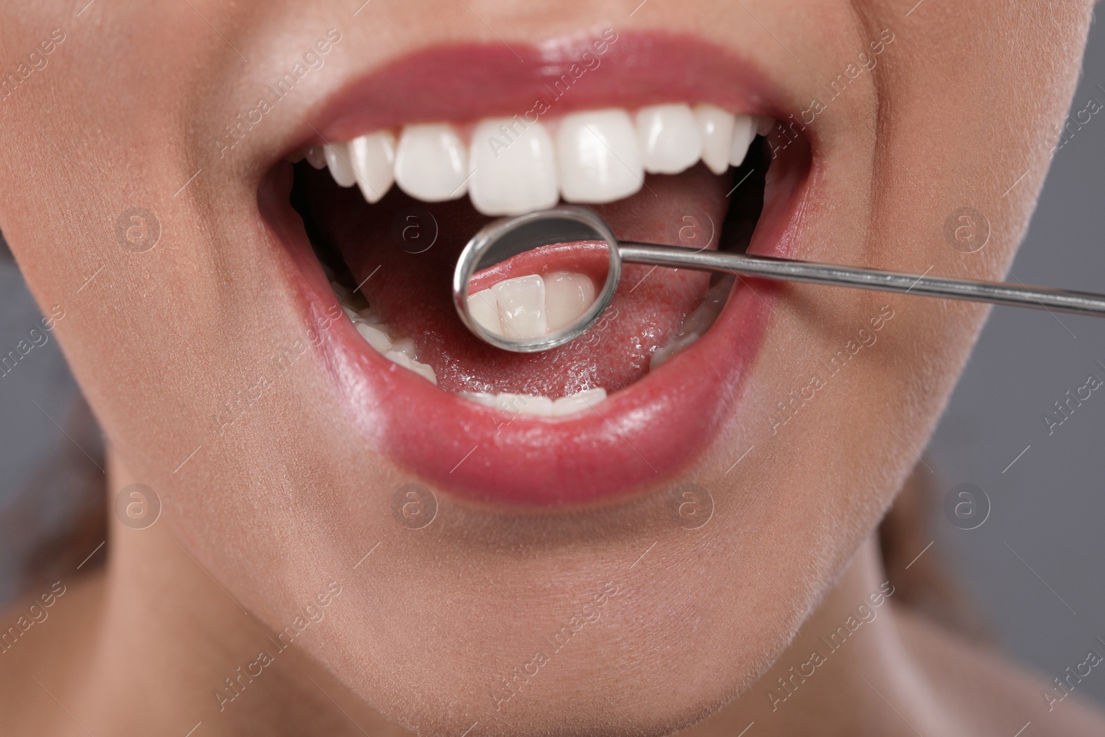 Photo of Examining woman's teeth with dentist's mirror on grey background, closeup