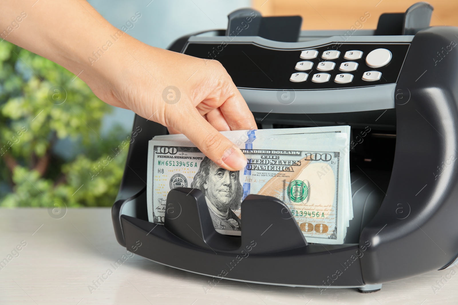 Photo of Woman taking money from counting machine at table indoors, closeup