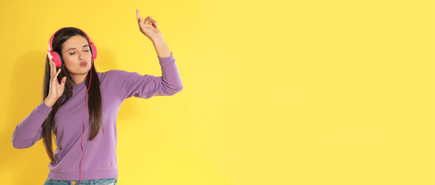 Young woman listening to music with headphones on yellow background, space for text. Banner design