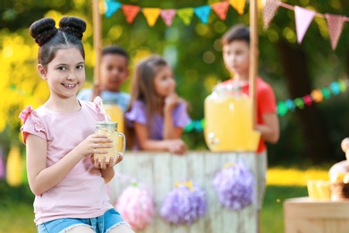 Cute little girl with natural lemonade in park, space for text. Summer refreshing drink
