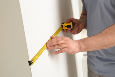 Photo of Man measuring white wall indoors, closeup. Construction tool