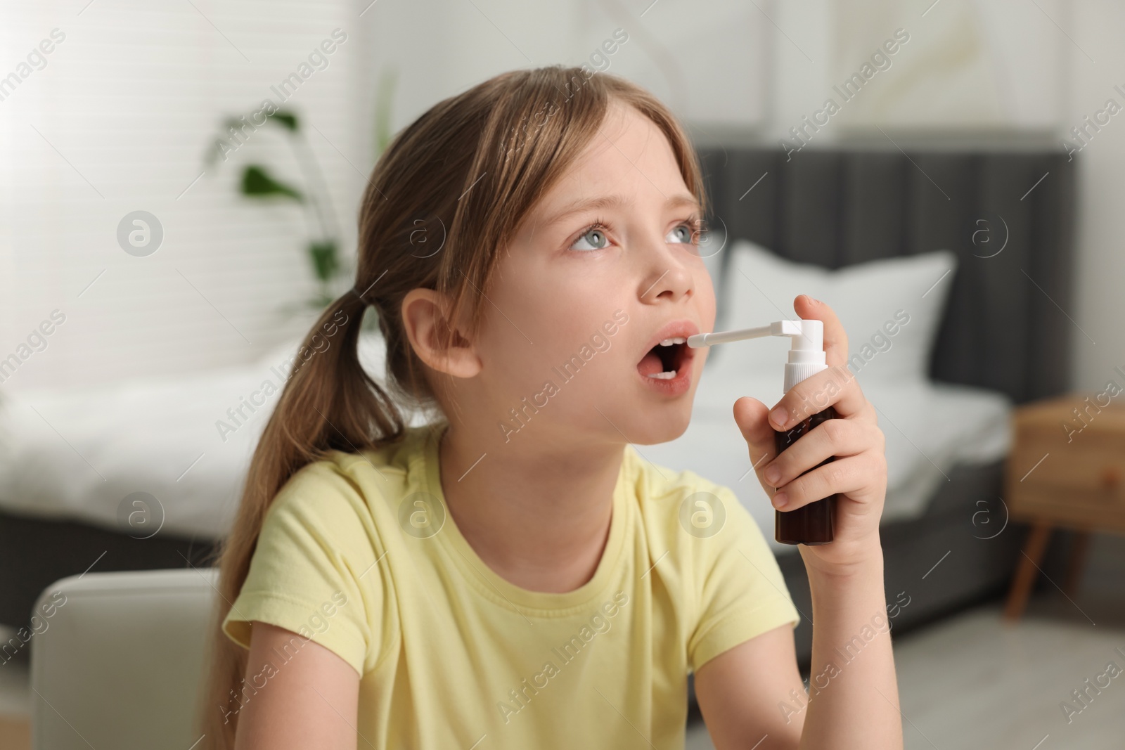 Photo of Little girl using throat spray at home