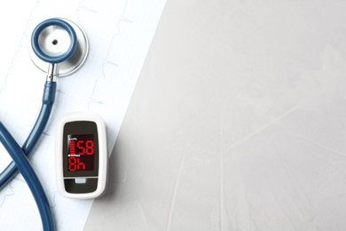 Modern fingertip pulse oximeter, stethoscope and cardiogram on grey stone table, flat lay. Space for text