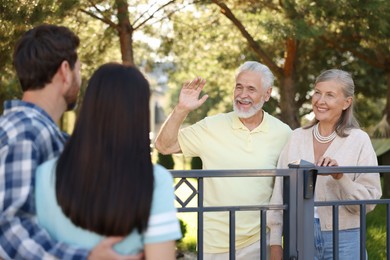 Photo of Friendly relationship with neighbours. Elderly couple greeting young family near fence outdoors