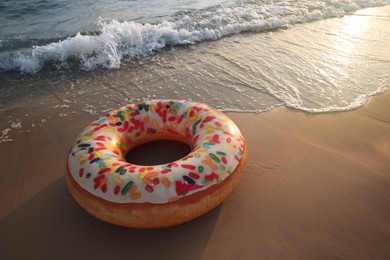 Photo of Inflatable ring with doughnut pattern on sunlit sandy beach near sea, space for text