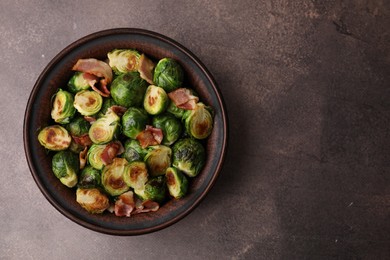 Photo of Delicious roasted Brussels sprouts and bacon in bowl on brown table, top view. Space for text