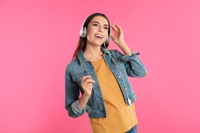 Beautiful young woman listening to music with headphones on color background