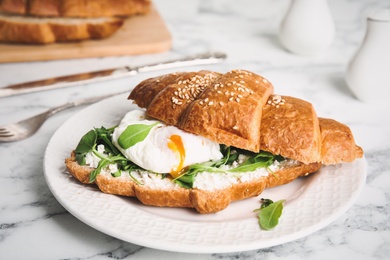 Photo of Delicious croissant with arugula and egg on white marble table, closeup