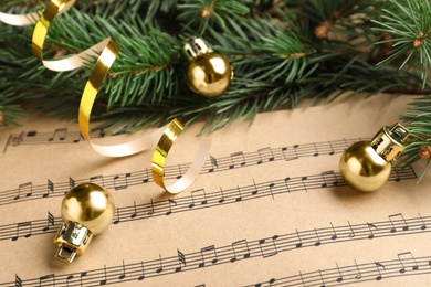 Photo of Fir branches, golden streamer and balls on Christmas music sheets, closeup