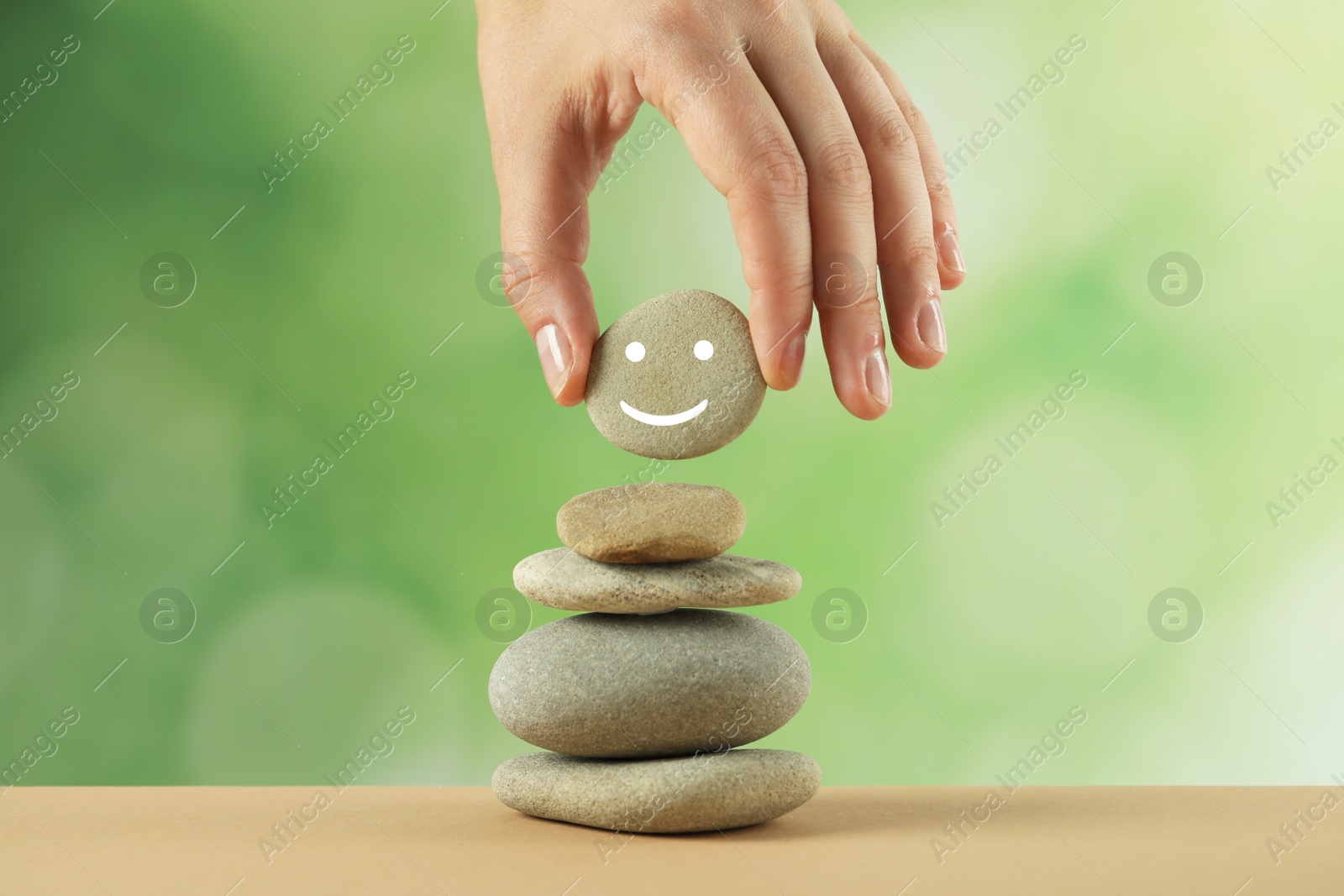 Photo of Woman putting stone with drawn happy face onto stack against blurred background, closeup. Zen concept