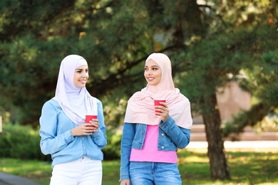 Photo of Muslim women with cups of coffee walking in park