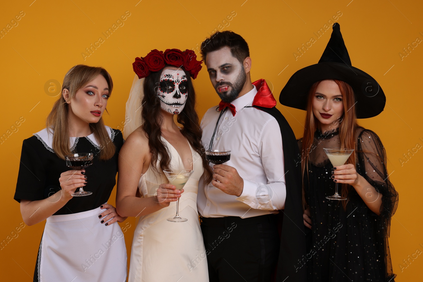 Photo of Group of people in scary costumes with cocktails on orange background. Halloween celebration