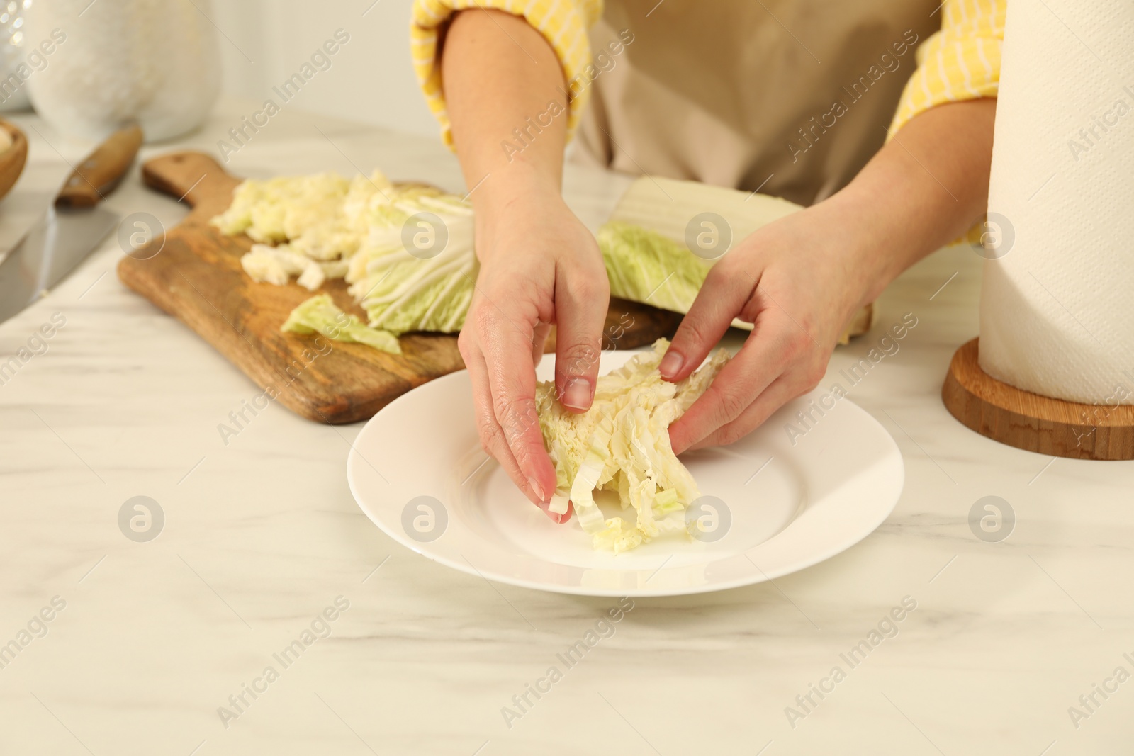 Photo of Woman putting cut Chinese cabbage into plate at white kitchen table, closeup