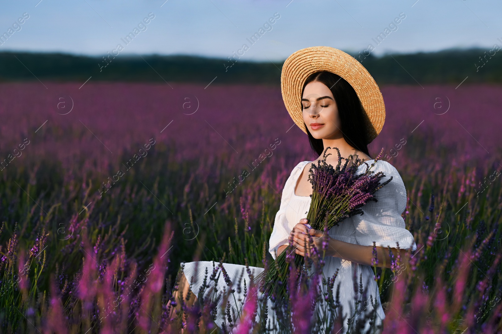 Photo of Beautiful young woman with bouquet sitting in lavender field