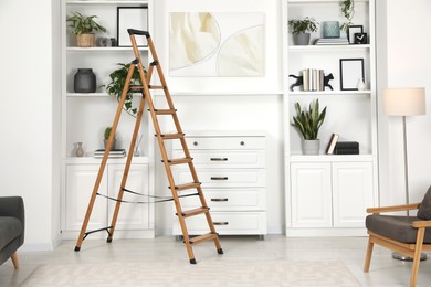 Wooden folding ladder near chest of drawers and shelves with accessories in room