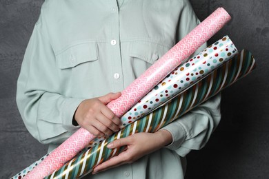 Photo of Woman holding different colorful wrapping paper rolls on grey background, closeup