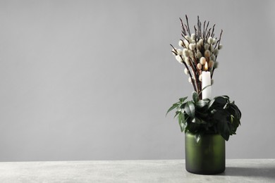 Photo of Burning candle, plant and willow branches on grey table, space for text