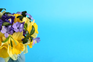 Photo of Bouquet of beautiful yellow daffodils, iris and periwinkle flowers in vase on light blue background. Space for text