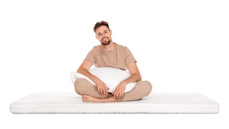 Photo of Smiling man with pillow sitting on soft mattress against white background