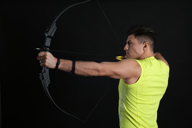 Photo of Man with bow and arrow practicing archery on black background
