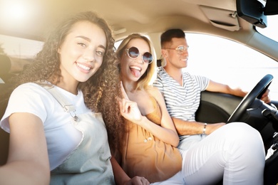Happy friends taking selfie in car on road trip