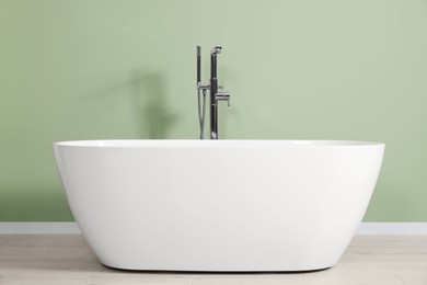 Photo of Modern ceramic tub near light green wall in bathroom. Interior design