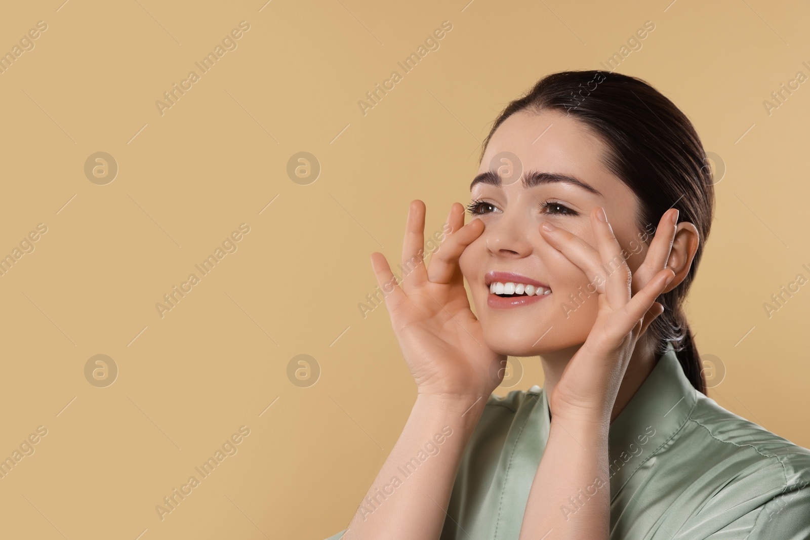 Photo of Young woman massaging her face on beige background. Space for text